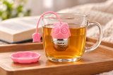 Pink owl infuser steeping in a glass mug with matching tray alongside
