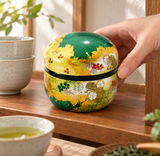 Green and gold floral tea container being placed on a tea shelf