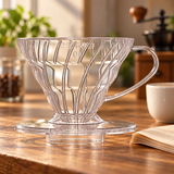 Transparent HARIO V60 01 dripper on a coffee preparation counter beside paper filters and a cup
