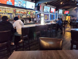 Dark Brown Upholstered Restaurant Barstool with Wood-Grain Metal Frame in a restaurant setting; other furniture is illustrative