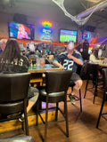 Dark Brown Upholstered Restaurant Barstool with Wood-Grain Metal Frame in a restaurant setting; other furniture is illustrative