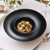 10¾″ Textured Black Ceramic Wide-Rim Bowl — 10 oz with risotto in the central well; table accessories shown separately