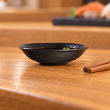 3¾-inch black ceramic shallow dish holding soy dipping sauce beside chopsticks
