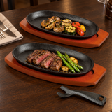 Two oval iron steak plates on wood bases with steak, vegetables and a removable holder