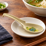 062-M beige and green patterned melamine soup spoon in a broth tasting setting