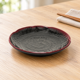 Dark round side dish with red rim on a dining table