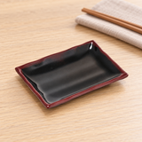 Dark rectangular side dish with red rim on a dining table
