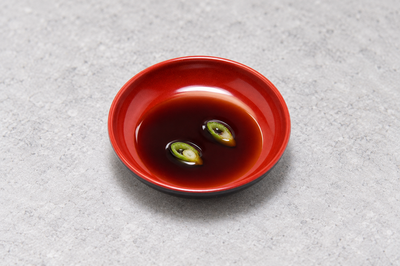 Round black and red sauce dish containing dark sauce with two green onion rings.
