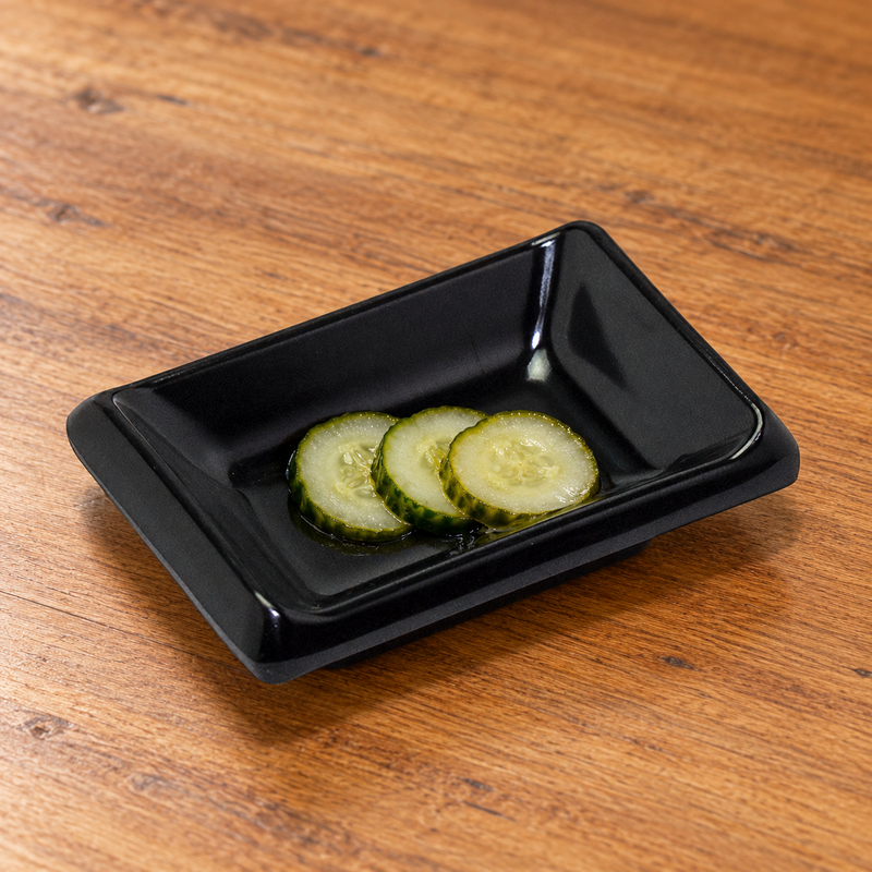 310/AB black rectangular melamine sauce dish with three small cucumber pickle slices, serving suggestion