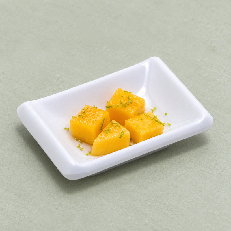 Golden mango pieces with a fine green garnish in the 310-W white rectangular dish on a pale green surface.