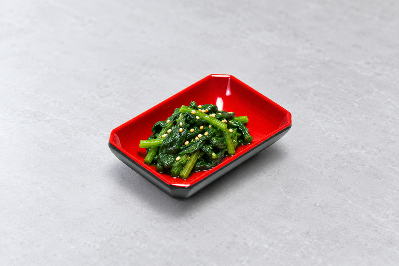 Rectangular black and red sauce dish holding leafy greens with pale sesame seeds.