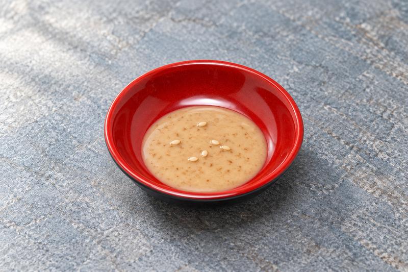 Round black and red sauce dish containing pale tan sauce with small seeds.