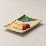 A pale cake slice with a powdered top and two raspberries on the 507-M rectangular patterned plate.