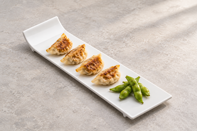 Serving suggestion with browned dumplings in a row and green edamame on the A15648 long white rectangular plate