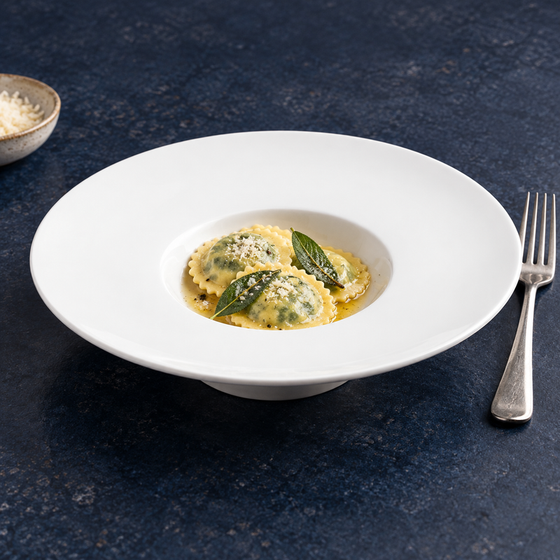 A2803 white wide-rim ceramic plate with ravioli, sauce, herbs and a grated topping as a serving suggestion.