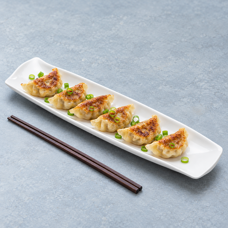Serving suggestion with a row of dumplings on the long white rectangular plate and chopsticks alongside.