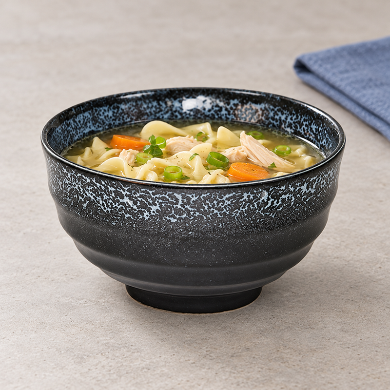 Black speckled bowl serving noodles, chicken, carrot and scallions