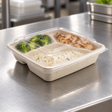 Three-compartment fiber to-go container with clear lid holding rice and two sides on a packing counter