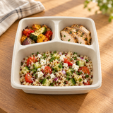 Open three-compartment fiber container with grain salad and sides on an oak dining table