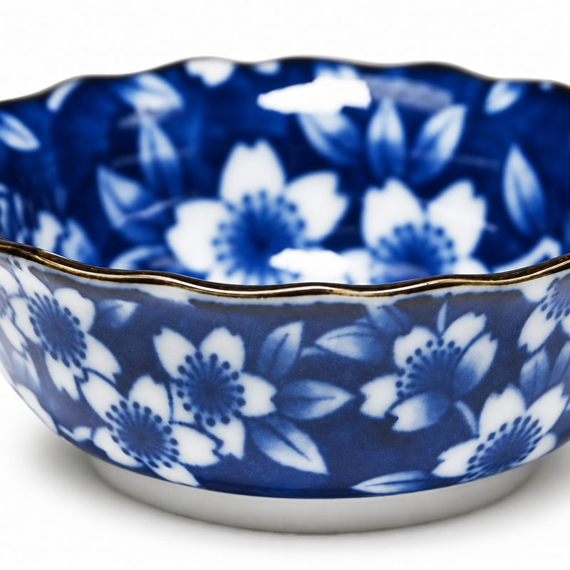 Close view of white sakura blossoms and pale leaves on the dark blue bowl, with a gently scalloped dark-edged rim.