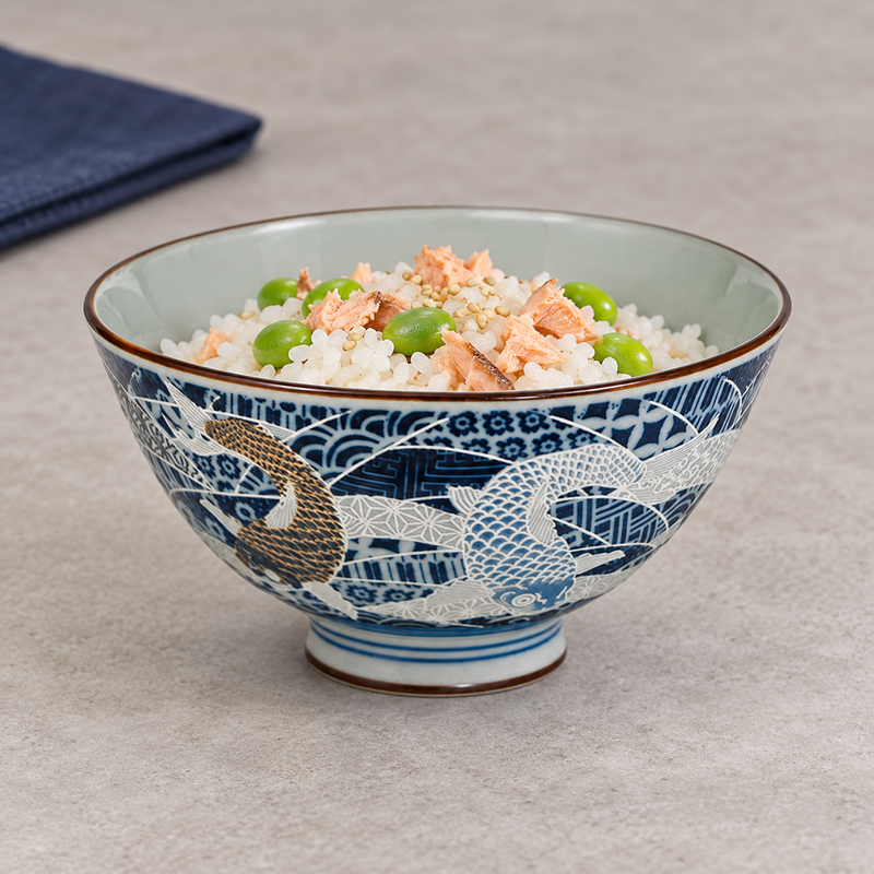 Blue koi bowl holding white rice with a light pink topping and green garnish, with a dark cloth nearby.