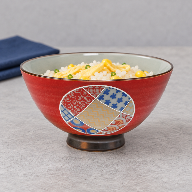Red patchwork rice bowl holding rice with yellow and green toppings on a gray tabletop.