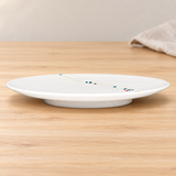 White footed plate with visible floral vine viewed from the side in a tabletop setting