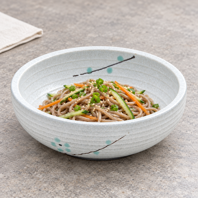 Wide white aqua-blossom porcelain bowl holding brown noodles with thin green and orange vegetable strips on a light surface.