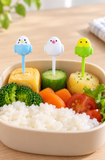 Three small bird food picks inserted by their stems into bite-size lunch portions