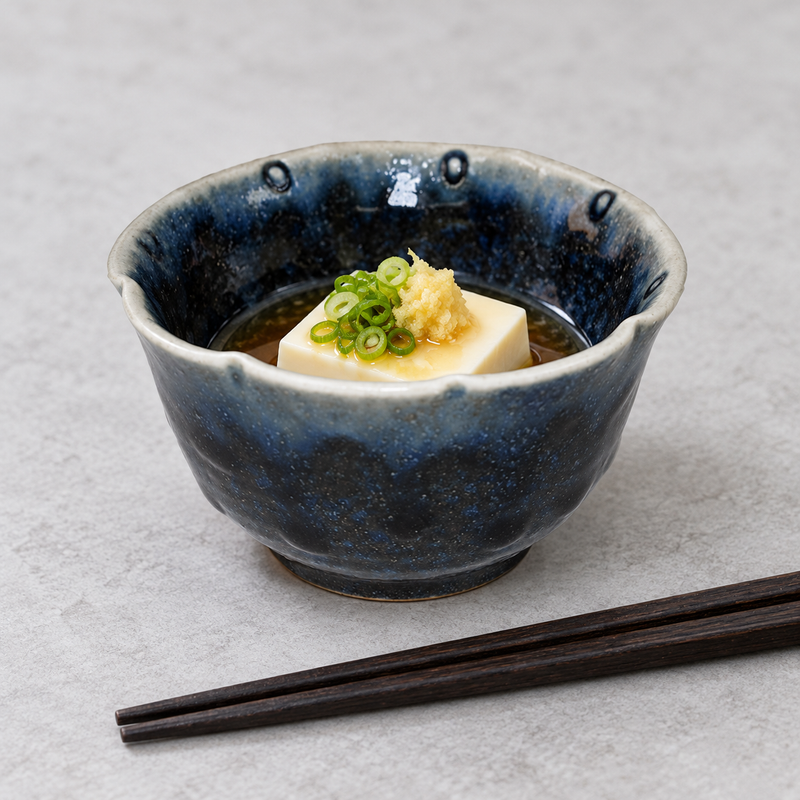 Navy ceramic small bowl holding a light tofu portion with green garnish, with chopsticks beside it.