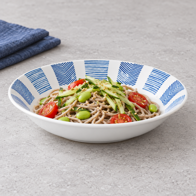 Serving suggestion with dressed soba noodles, cucumber, tomatoes and edamame in the blue geometric shallow bowl.