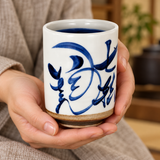 KA70-6 white and blue calligraphic tea cup supported in hands