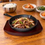 NTP-08 cast iron steak pan on dark serving base — beef and onion serving suggestion