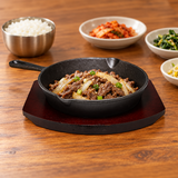 NTP-09 cast iron steak pan on dark serving base — beef and onion serving suggestion