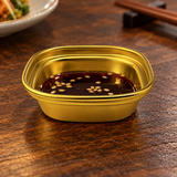 SSG-SAP1-3 single-well gold sauce dish with dipping sauce on a restaurant table