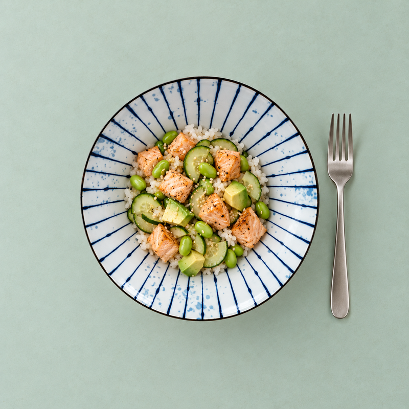 Overhead KF570-FU bowl with white rice, orange fish-like cubes, cucumber rounds, avocado chunks, green beans and sesame, with a metal fork outside right.