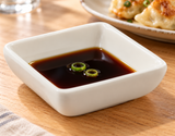 M334 ivory square melamine sauce dish with soy sauce and scallion rings.