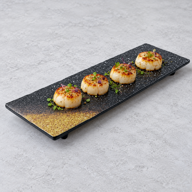 Seared scallops arranged in a line on the dark speckled platter