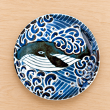 Whale and blue wave ceramic plate on a pale wooden tabletop