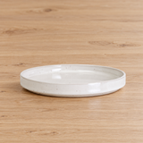White shallow round ceramic plate on a pale wooden table