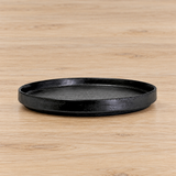 Black shallow round ceramic plate on a pale wooden table