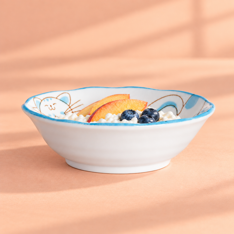 Blue cat-pattern ceramic bowl with a creamy-white base, two red-skinned orange-yellow fruit slices and blueberries; no utensil is shown.
