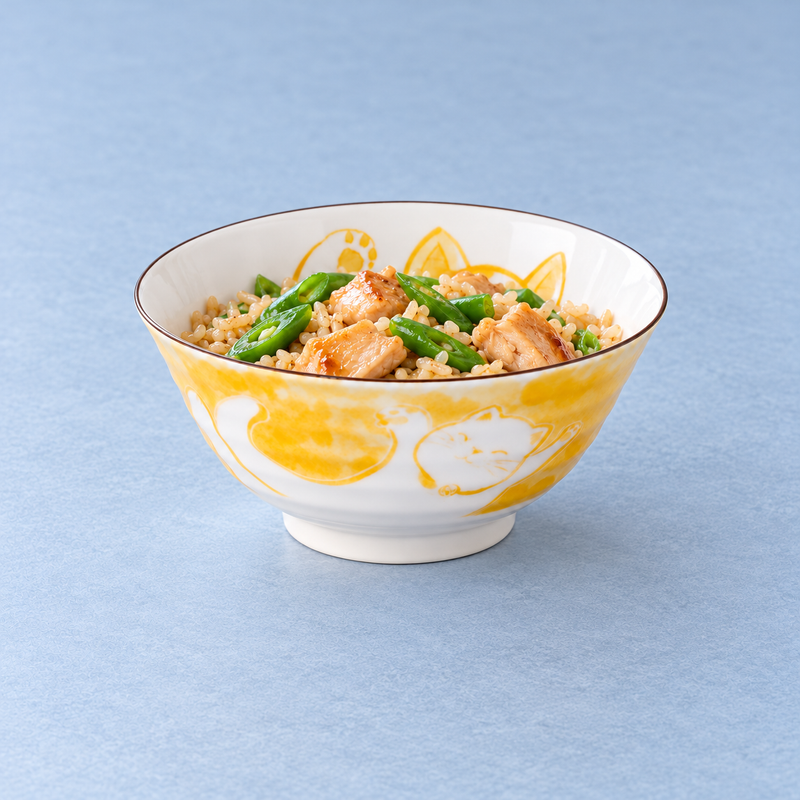 MT56-MCY yellow cat bowl holding rice with browned meat pieces and green vegetables on a blue tabletop