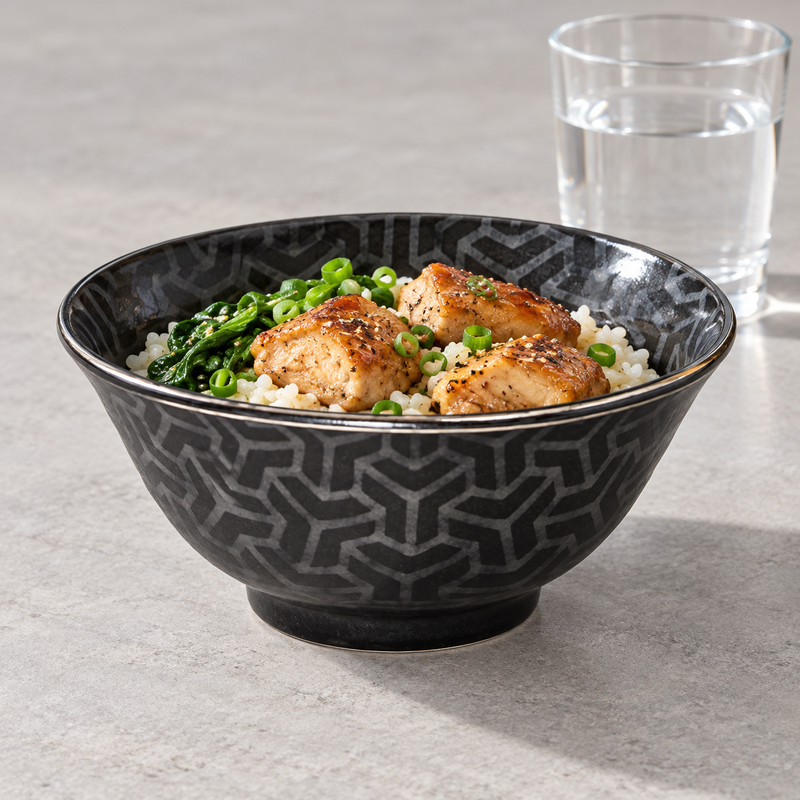 MY56-GKK patterned bowl with rice, three browned meat pieces, leafy greens and scallions; a water glass is behind-right and no utensil is shown.