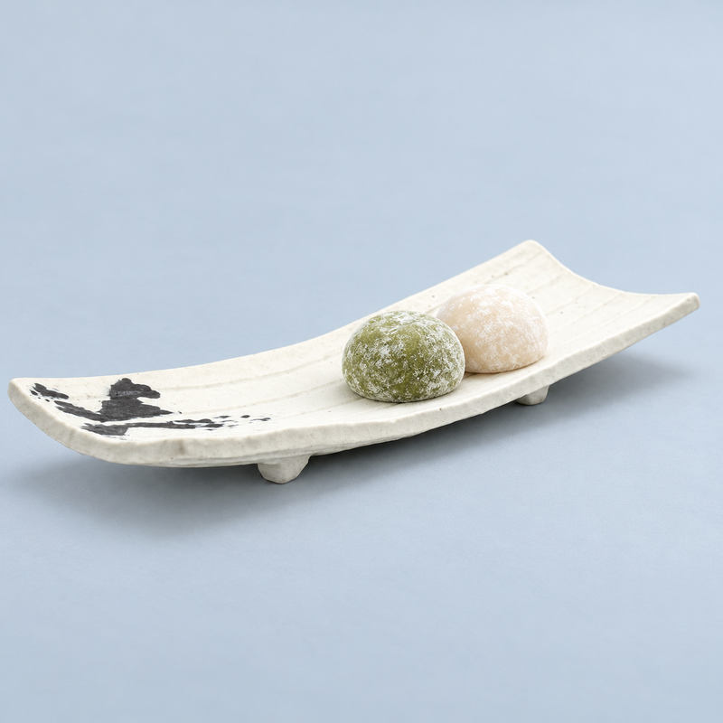 White elongated porcelain plate with black end decoration holding two powdered rounded sweets, one green and one cream-colored.