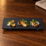 Black rectangular footed melamine plate presenting mushroom appetizers on a walnut table