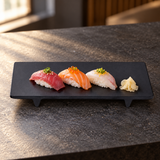 Black rectangular footed melamine plate with three nigiri pieces on a charcoal counter