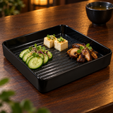 Black square ridged-base melamine plate presenting separate tofu, cucumber and mushroom appetizers