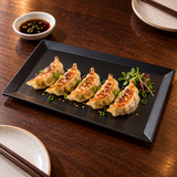 Black rectangular melamine plate holding gyoza for sharing at a walnut restaurant table