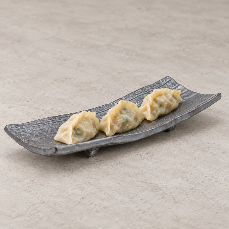 Black elongated porcelain plate with raised ends and lengthwise ridges, holding three pale folded dumplings.
